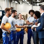 Company managers visiting their employees in a factory. Happy African American businesswoman is shaking hands with one worker.